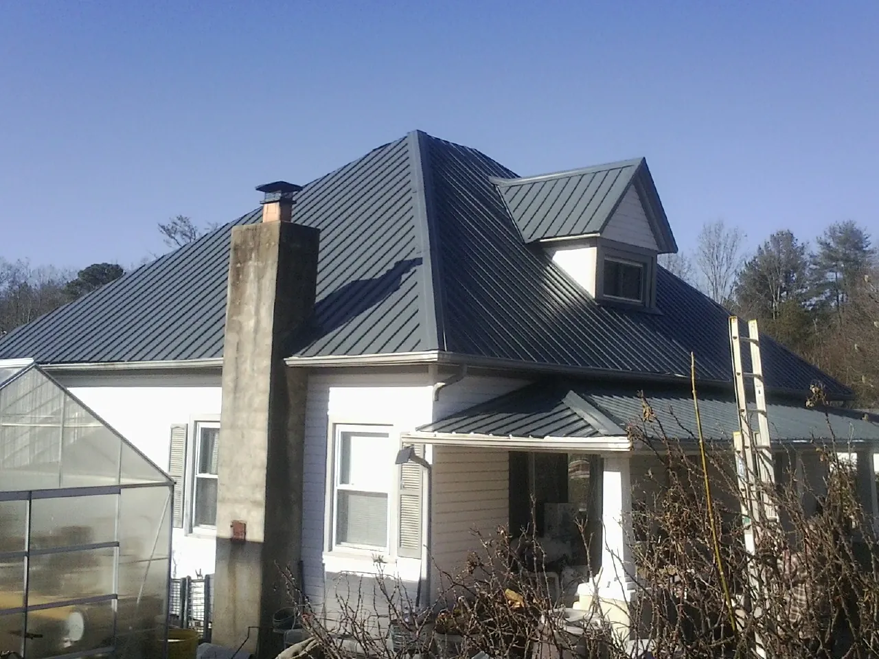 Dark blue standing seam metal roof on a white farmhouse with dormer — Slate & Tile Roof Repair by Roofing Brothers in Brookston