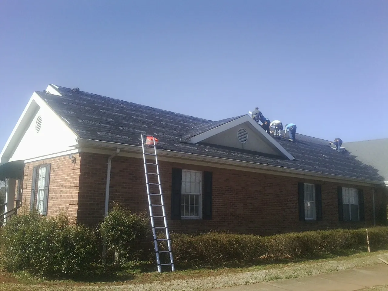 Crew tearing shingles off a brick ranch roof with a ladder set — Emergency Roof Repair work by our crew in Brookston