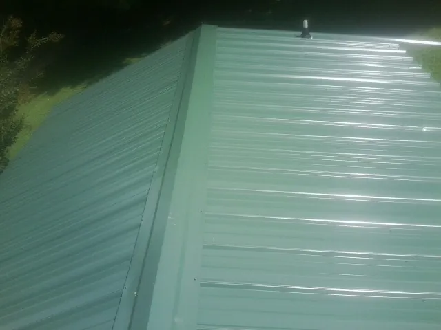 New green metal panels meeting at the ridge of a roof — Flat Roof Repair work by our crew in Brookston