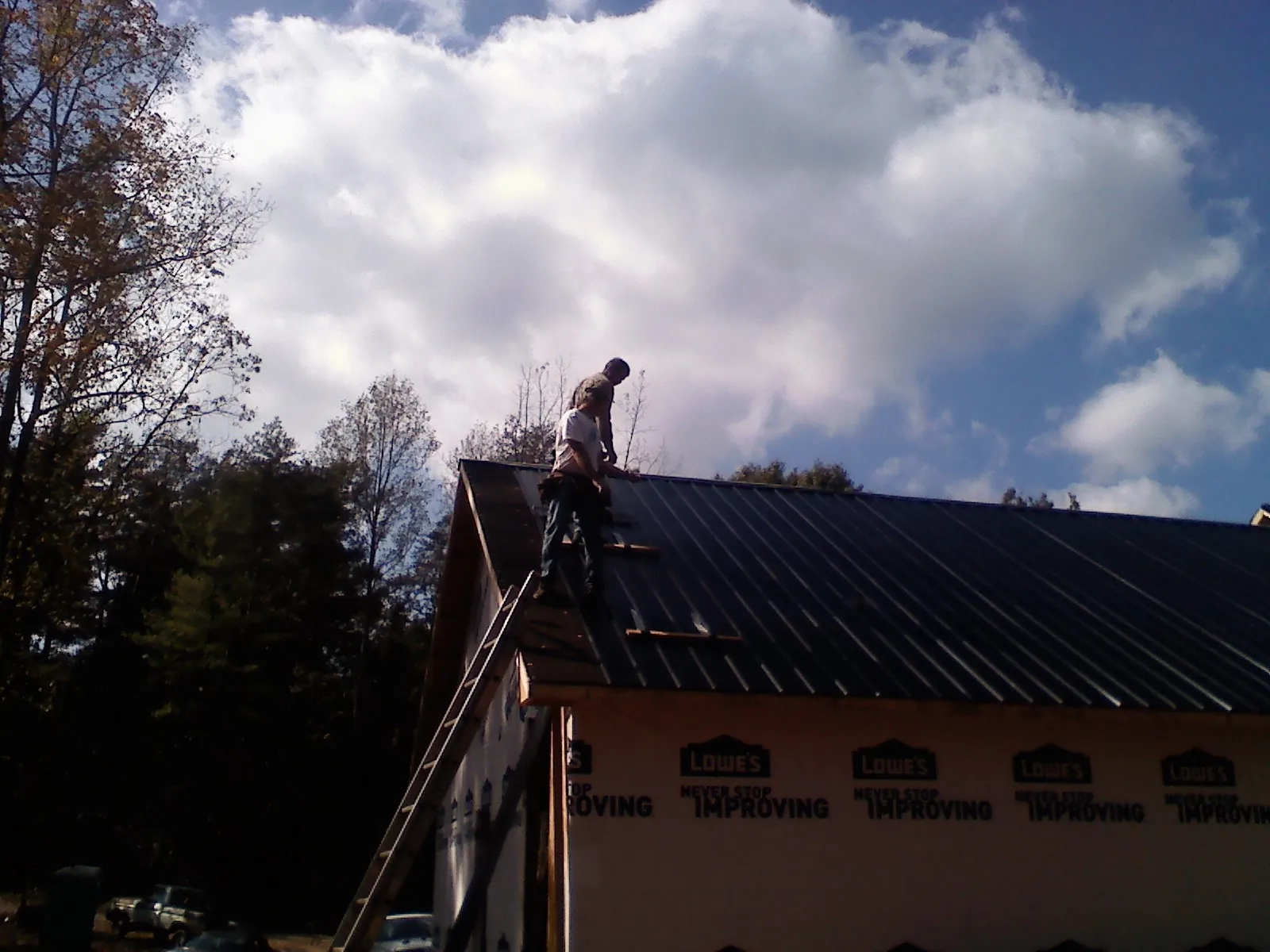 Roofer fastening dark metal panels high against a cloudy sky, from a Roof Inspection job in Brookston