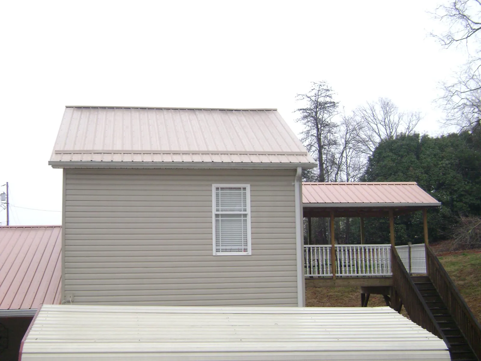 Tan metal roofs on a two story addition and attached porch, from a Roof Replacement job in Brookston